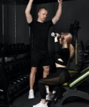 Fitness instructor conducts personal training for a girl with dumbbell in front of the mirror